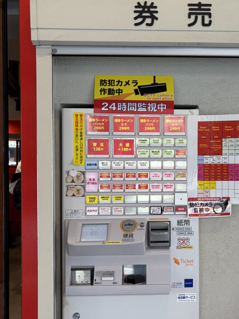 A traditional Japanese ramen shop ticket machine with physical buttons and a cash slot for coins and yen bills.